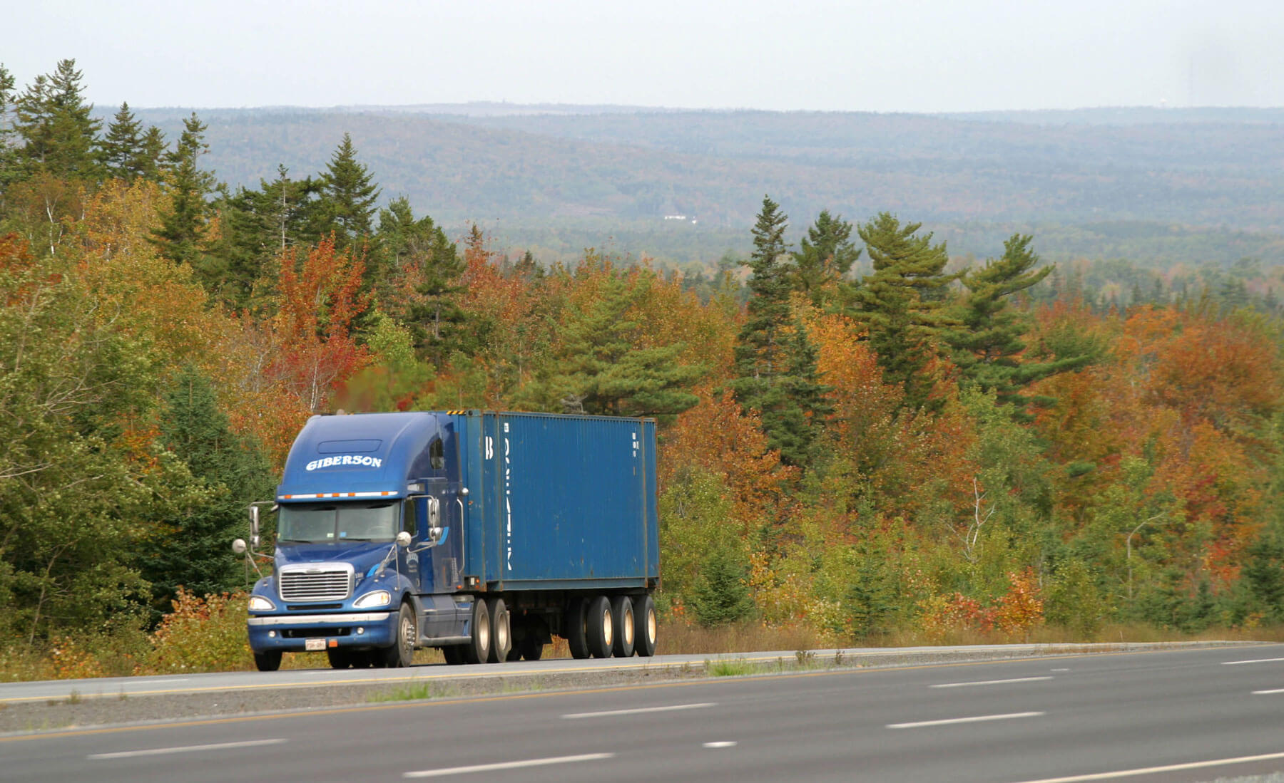 A blue transport truck travels on Highway 102 in fall.