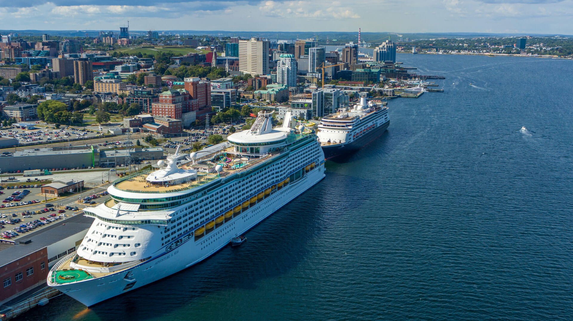 Aerial of two cruise ships moored near Pier 21. In the background is a sweeping aerial of downtown Halifax, Citadel Hill, and the Macdonald Bridge.