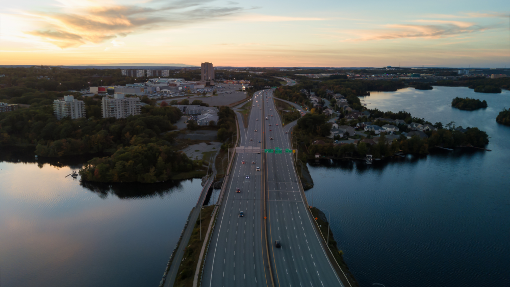 An aerial view of the Circumferential Highway at Lake Banook / Lake MicMac, with Micmac Mall in the background at sunset.